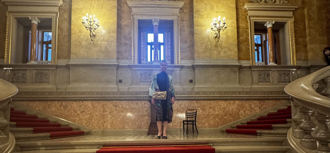 Grand staircase inside the Hungarian State Opera House in Budapest, with marble columns, gold details, and red carpet.