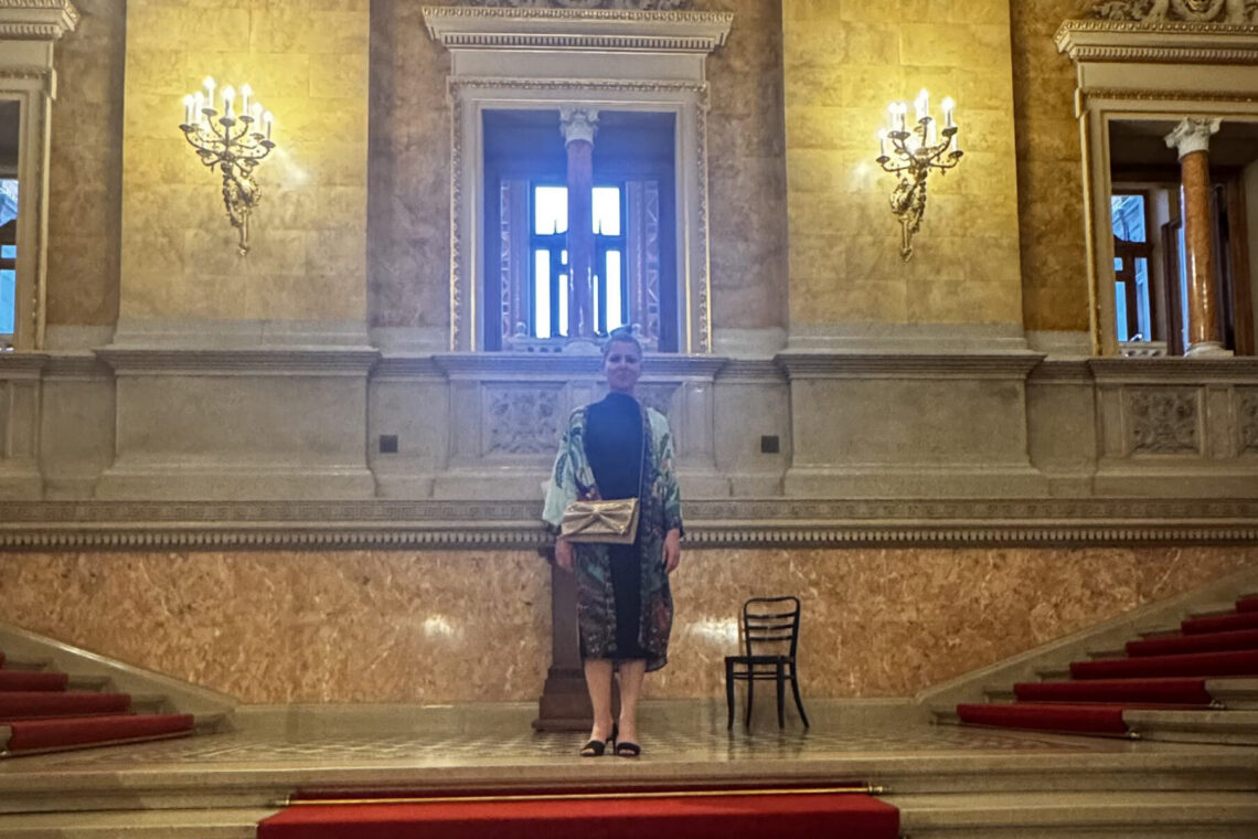 Grand staircase inside the Hungarian State Opera House in Budapest, with marble columns, gold details, and red carpet.