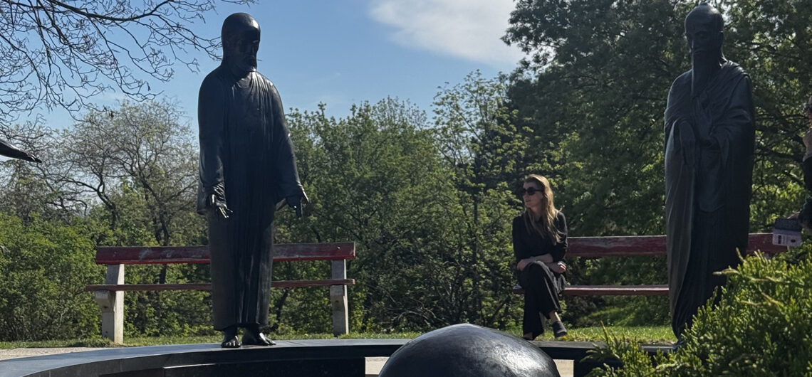 Quiet moment in Philosophers Garden Budapest with statues and a visitor relaxing on a bench among trees