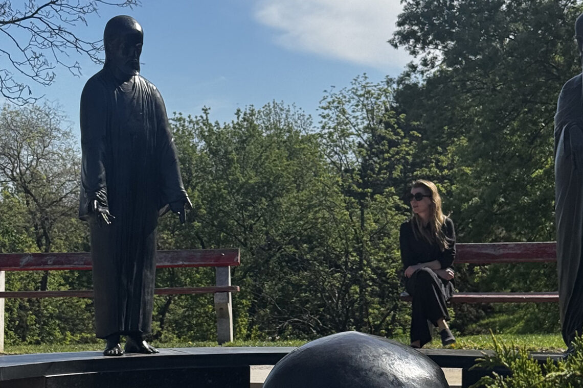 Quiet moment in Philosophers Garden Budapest with statues and a visitor relaxing on a bench among trees